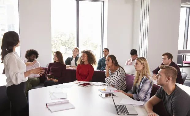 Des personnes sont dans une classe et écoutent attentivement l'intervenante.  