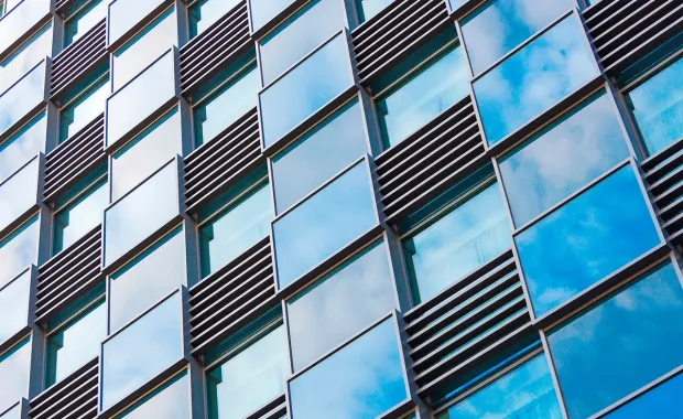 Glasfront eines Bürogebäudes, indem sich Wolken widerspiegeln