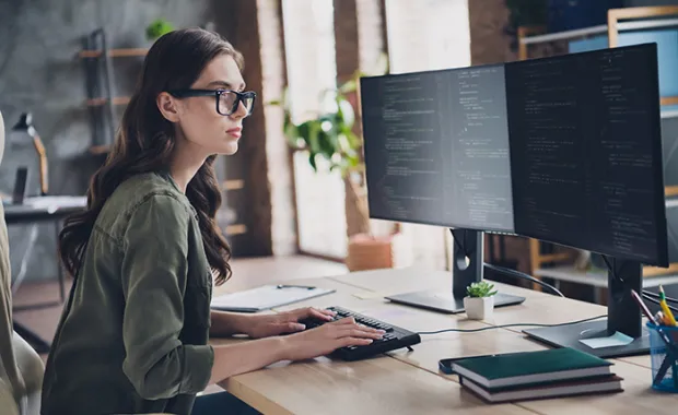 A professional businesswoman sitting at a computer looking at code 