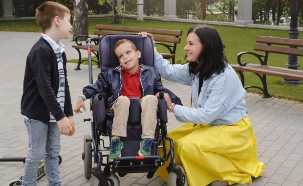  A woman and a boy, along with a child in a wheelchair, are engaged in a joyful conversation