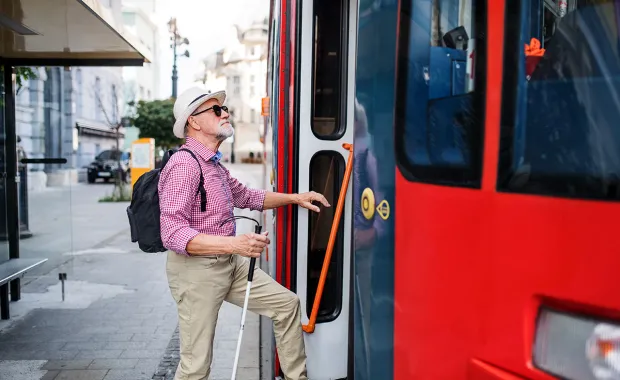 En blind man med en käpp kliver på en röd buss