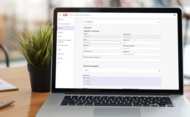 En bärbar dator som visar ett formulär på en webbplats med CGI logotyp, där användaren fyller i personuppgifter för en ansökan om statligt stöd. Datorn står på ett skrivbord bredvid en grön krukväxt.