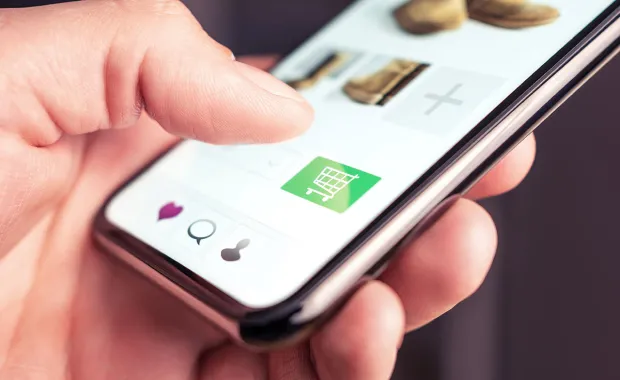 Hand som trycker på en grön kundvagnsikon på en smartphone, vilket indikerar köp på en e-handelsapp