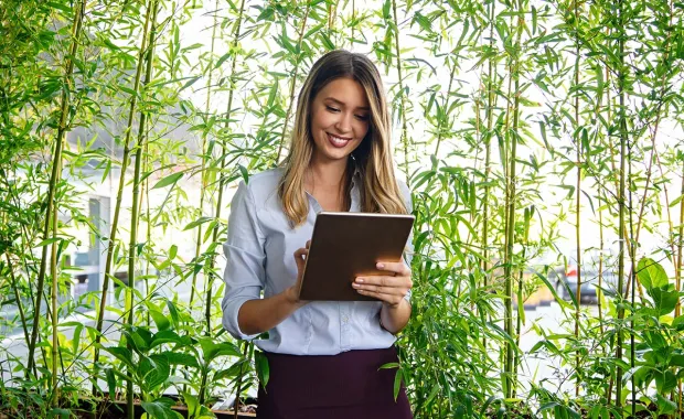 person holding a tablet, standing amidst green plants