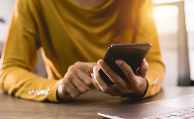 Kvinna i gul tröja sitter och knappar på sin mobiltelefon
