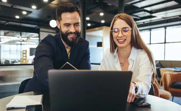 Two professionals smiling and looking at a laptop