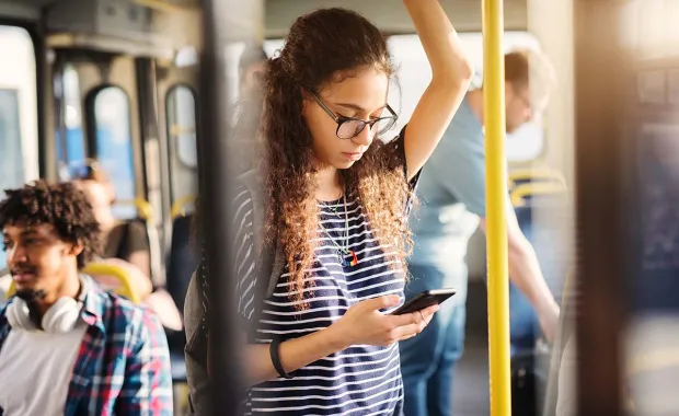 Girl standing on a bus looking at her phone