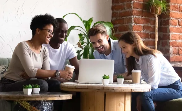 A group of diverse individuals laughing and looking at a laptop
