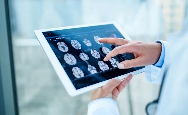 male clinician’s hands reviewing a brain scan on a tablet device