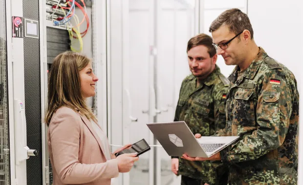 3 CGI Member stehen in einem Rechenzentrum, zwei davon tragen eine Bundeswehruniform