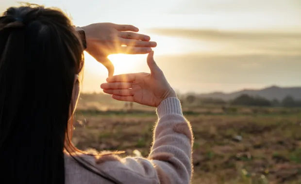 mujer enmarcando el sol con sus manos
