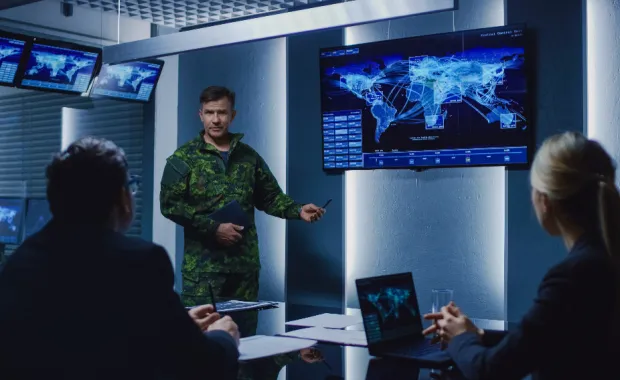 Military personnel having a meeting in front of computer screen and laptops