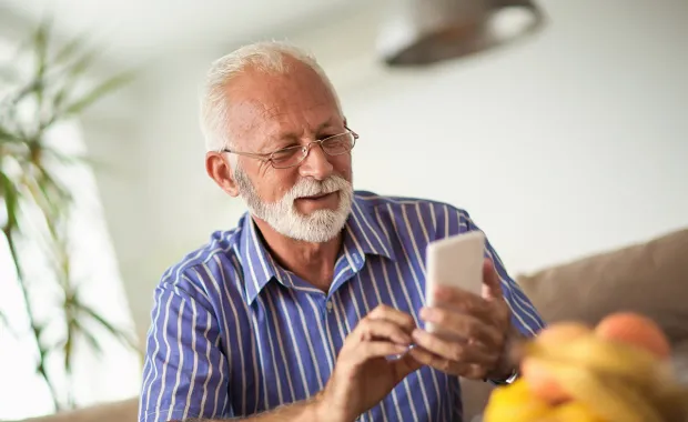 Pensionär anvander smartphone med två händer och ler