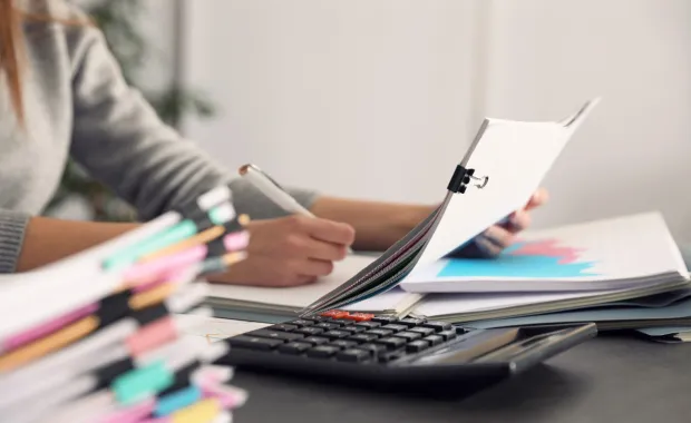 person checking paperwork and commissions figures at a desk with a calculator 