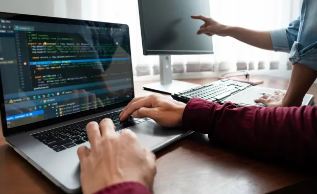 Two people working on a laptop and computer monitor