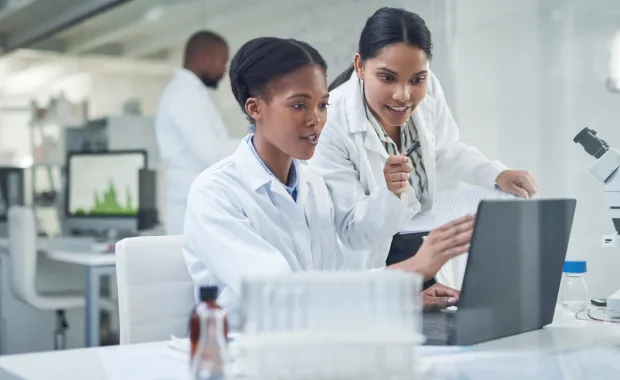 Two professionals in lab coats looking at a computer