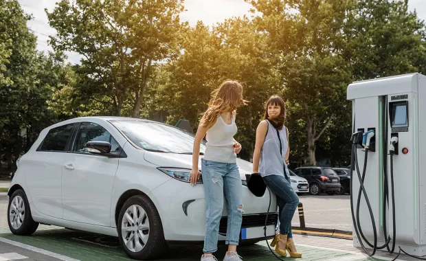 Two young women chatting while standing next to a charging EV