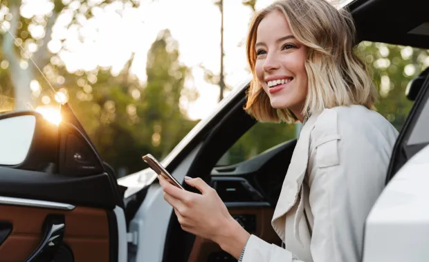 Junge Frau steigt mit einem Handy in der Hand aus einem Auto aus.