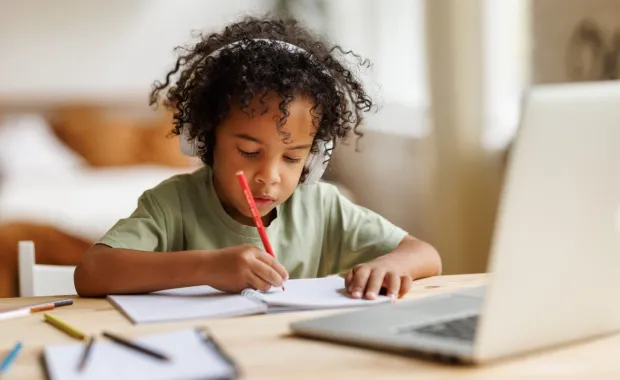 A young child wearing headphones writing on a notepad