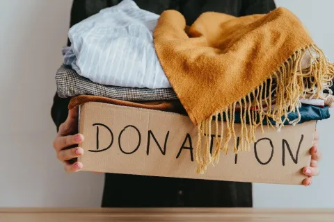 A person holding a box labeled donation and filled with clothes.