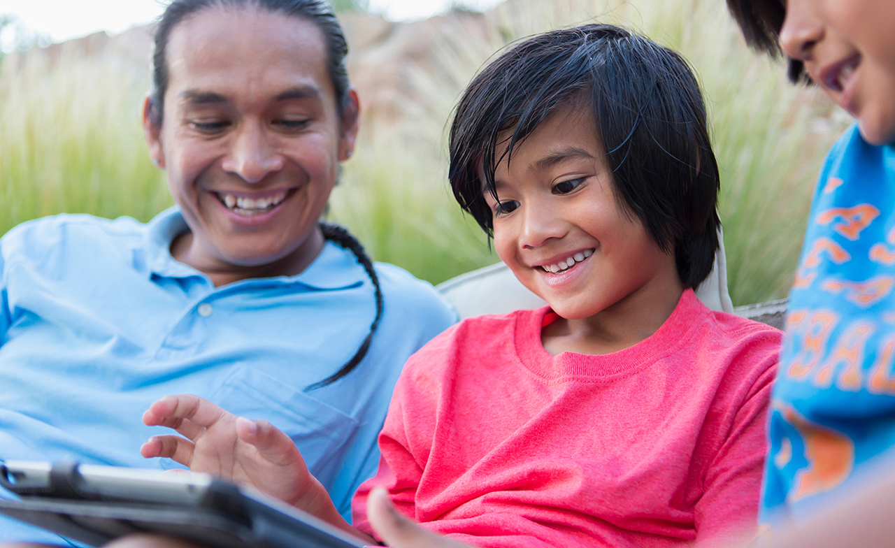 Smiling children and adult using a tablet in a field of grass