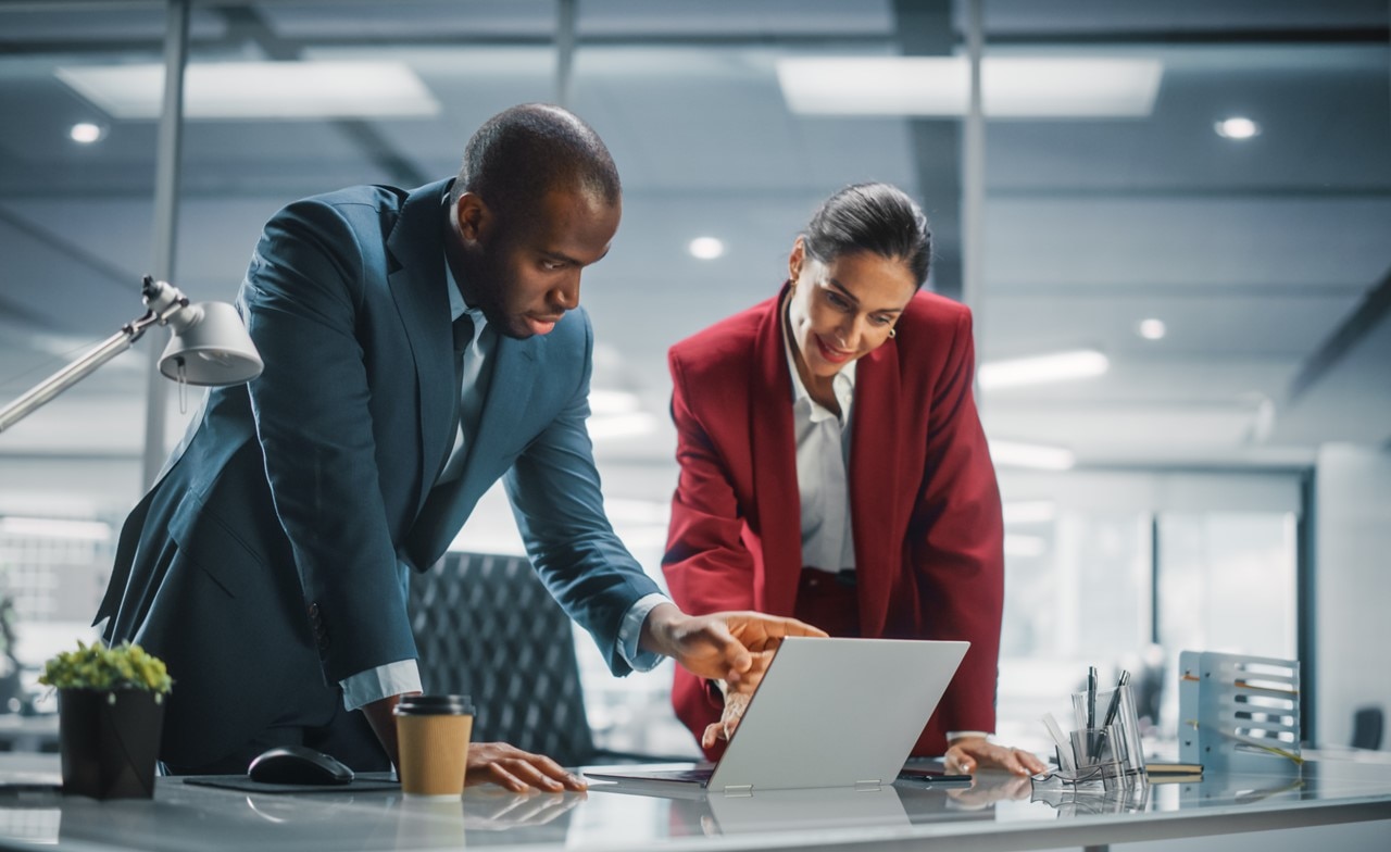 Two professionals standing and talking while looking at a computer