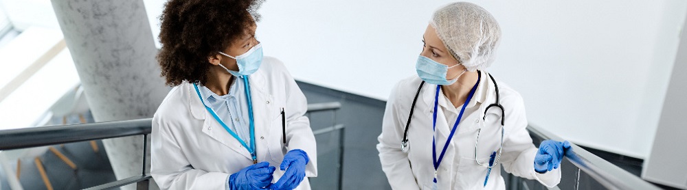 Två kvinnliga läkare med munskydd går uppför en trappa