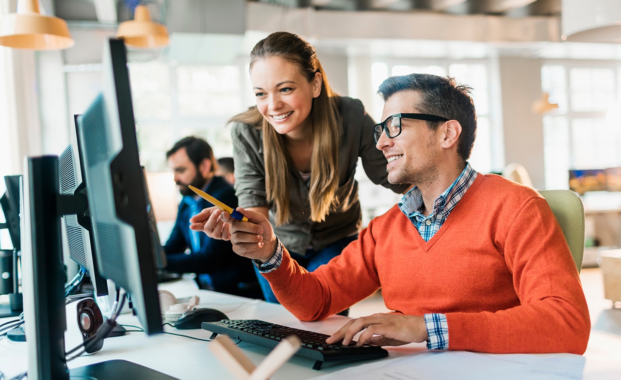 To personer smiler foran laptop – viser teamsamarbeid i utviklingsprosjekt To personer smiler foran laptop – viser teamsamarbeid i utviklingsprosjekt