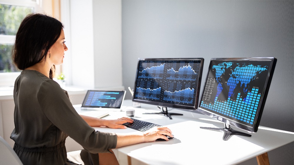 Woman working with data on multiple computer monitors